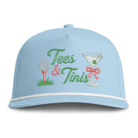 Load image into Gallery viewer, A light blue baseball cap with embroidered 'Tees &amp; Tinis' text, a golf ball on a tee, and a martini glass with a red bow on the front.