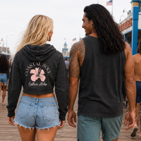 Load image into Gallery viewer, A woman and a man walking away on a boardwalk, both wearing dark charcoal hoodies. The back of the hoodie features a pink hibiscus flower graphic with the text 'COASTAL SOUL' and 'Endless Aloha' in pink.