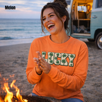 Load image into Gallery viewer, Laughing brunette woman with highlights in a messy bun clapping her hands by a beach campfire at dusk wearing a melon Lucky faux patch long sleeve shirt with a surf van behind her