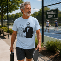 Load image into Gallery viewer, Gray-haired man wearing light blue Lob Father pickleball shirt standing beside outdoor pickleball courts with paddle and water bottle.