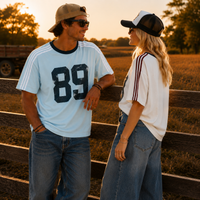 Load image into Gallery viewer, A man and a woman standing outdoors at sunset near a wooden fence, wearing matching white graphic t-shirts with dark lettering and striped shoulder details, paired with jeans and trucker-style caps.