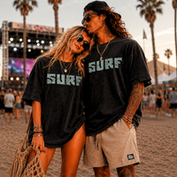 Load image into Gallery viewer, Oversized Cali Surf graphic t-shirt worn by a couple at a beach music festival during golden hour featuring retro California surf artwork.