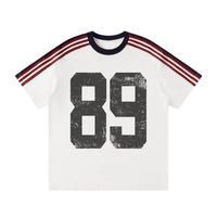 Load image into Gallery viewer, A white short-sleeve ringer T-shirt featuring a distressed black '89' graphic on the front, with navy and red three-stripe detailing on the shoulders and collar.
