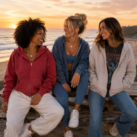 Load image into Gallery viewer, Three women sitting together on a wooden boardwalk by the beach at sunset, wearing casual zip-up hoodies and jackets in red, blue, and light gray.