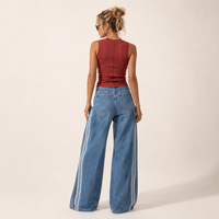 Load image into Gallery viewer, A woman shown from the back wearing a sleeveless burgundy top and wide-leg blue jeans with white side stripes, photographed against a plain light beige studio background.