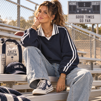 Load image into Gallery viewer, Woman wearing navy oversized unisex Varsity Stripe Heavyweight Pullover with faded jeans on football bleachers.