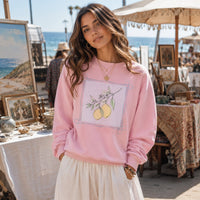 Load image into Gallery viewer, Lady in Pink cottage core crew neck sweatshirt with lemons on the front is browsing in a beachfront art gallery.