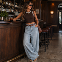 Load image into Gallery viewer, A woman stands at a wooden bar in a dimly lit pub, wearing a brown ribbed crop top with white trim, light-wash wide-leg jeans, and carrying a brown shoulder bag.